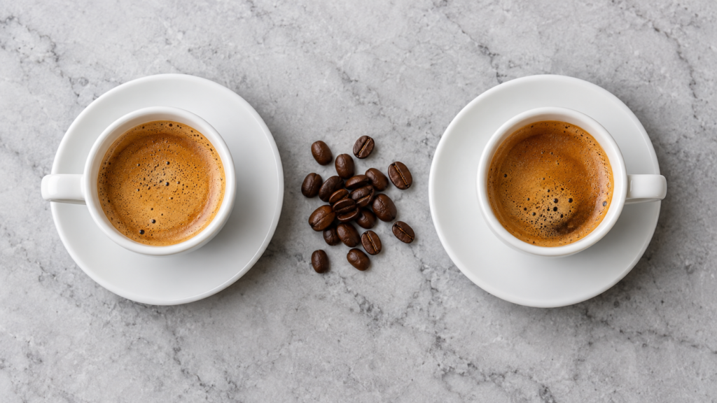 Duas xícaras de espresso com crema dourada posicionadas lado a lado sobre uma bancada de mármore representando a comparação entre as cafeteiras Philco e Mondial.