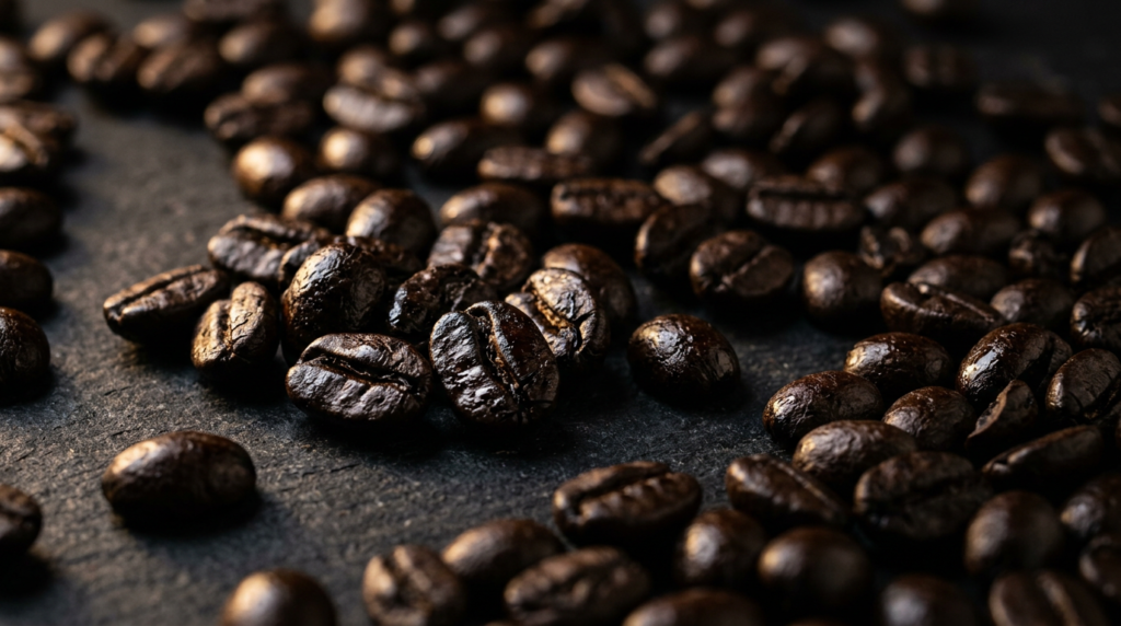 Grãos de café com torra escura, superfície visivelmente oleosa e coloração próxima ao preto.
